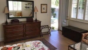Um quarto com cômoda, cama com roupa de cama florida, espelho e porta para uma varanda.