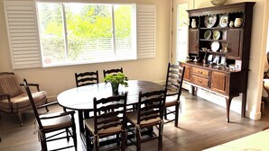 Uma sala de jantar com uma mesa redonda, seis cadeiras e um aparador com pratos decorativos.