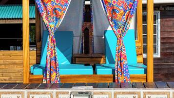 Un área de descanso junto a la piscina con cortinas coloridas y una estructura de madera.