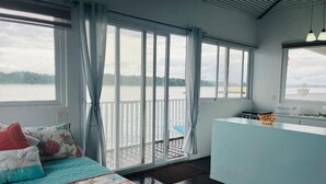 A room with a bed, a small kitchenette, and a view of a body of water through large windows. - Coral Wing Casitas (Bastimentos)