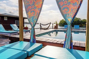 Un área junto a la piscina con sillones, una hamaca y una terraza de madera con vista al agua.