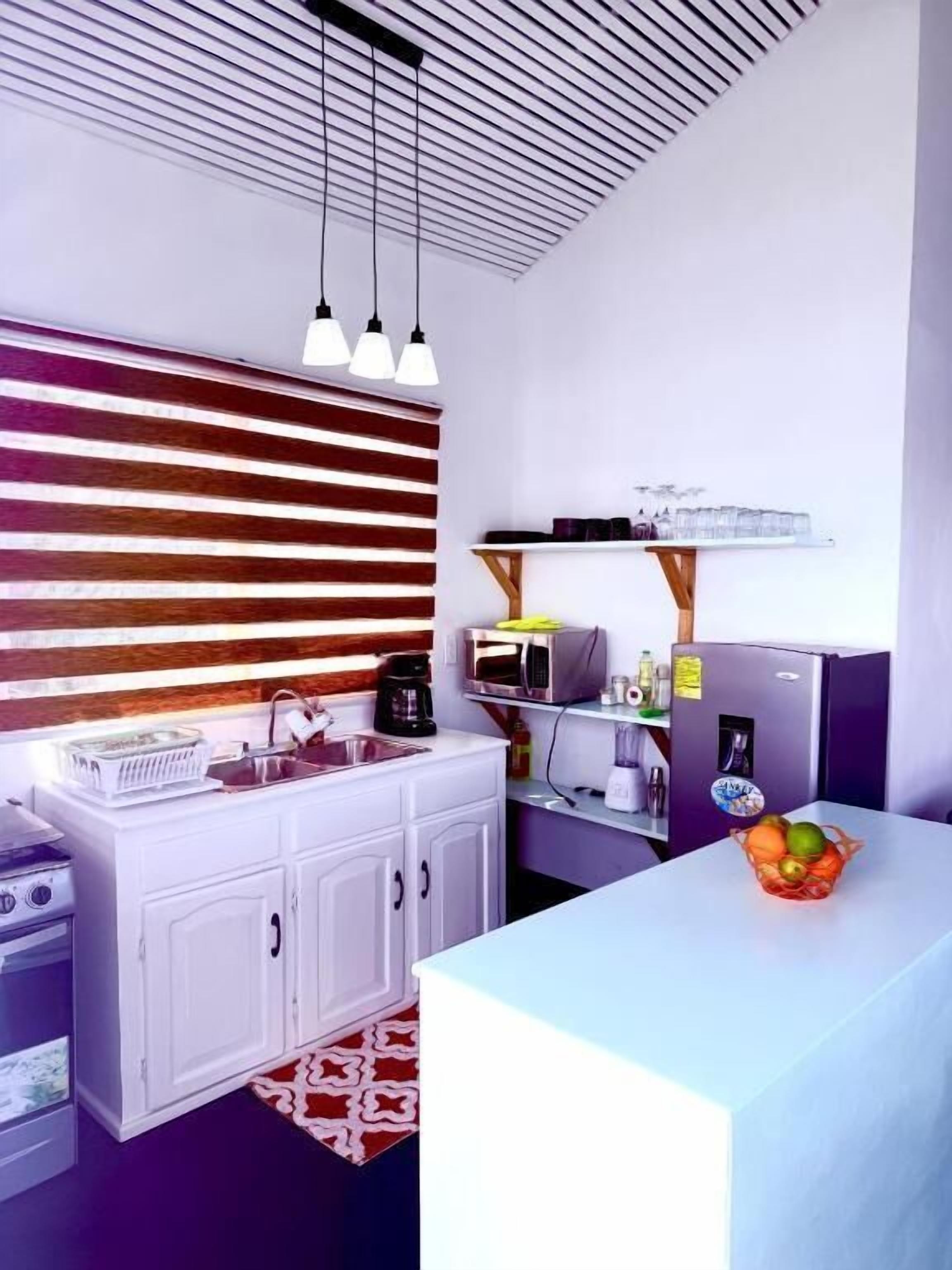 A compact kitchen with a white countertop, a built-in microwave, a coffee maker, and a fruit bowl.