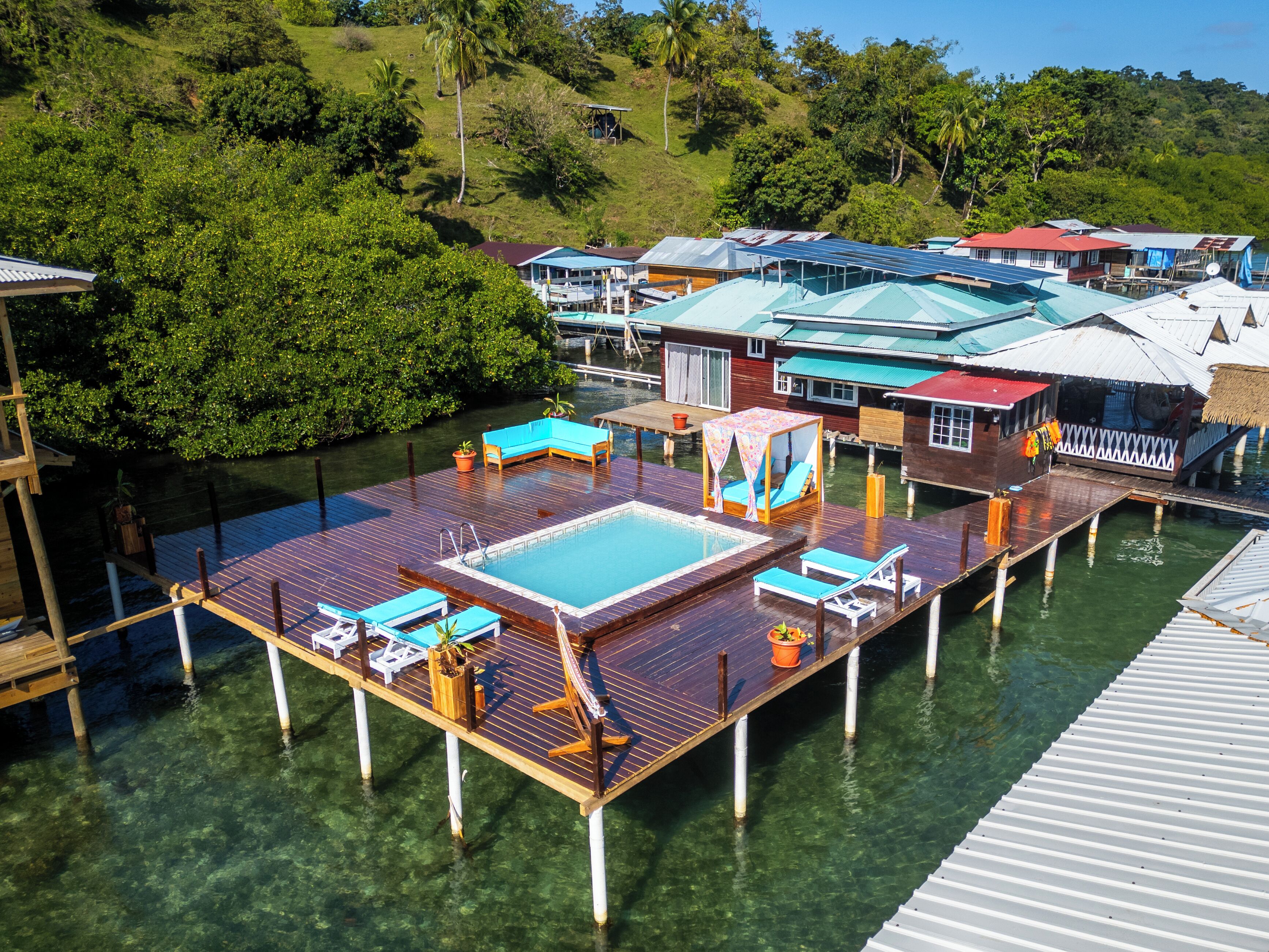 Een drijvend resort met een zwembad, ligbedden en houten steigers over het water.