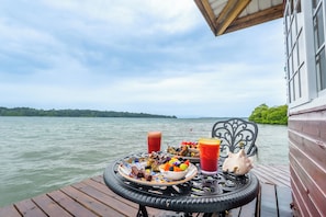 Una mesa con comida y bebidas en una terraza de madera junto a un lago.