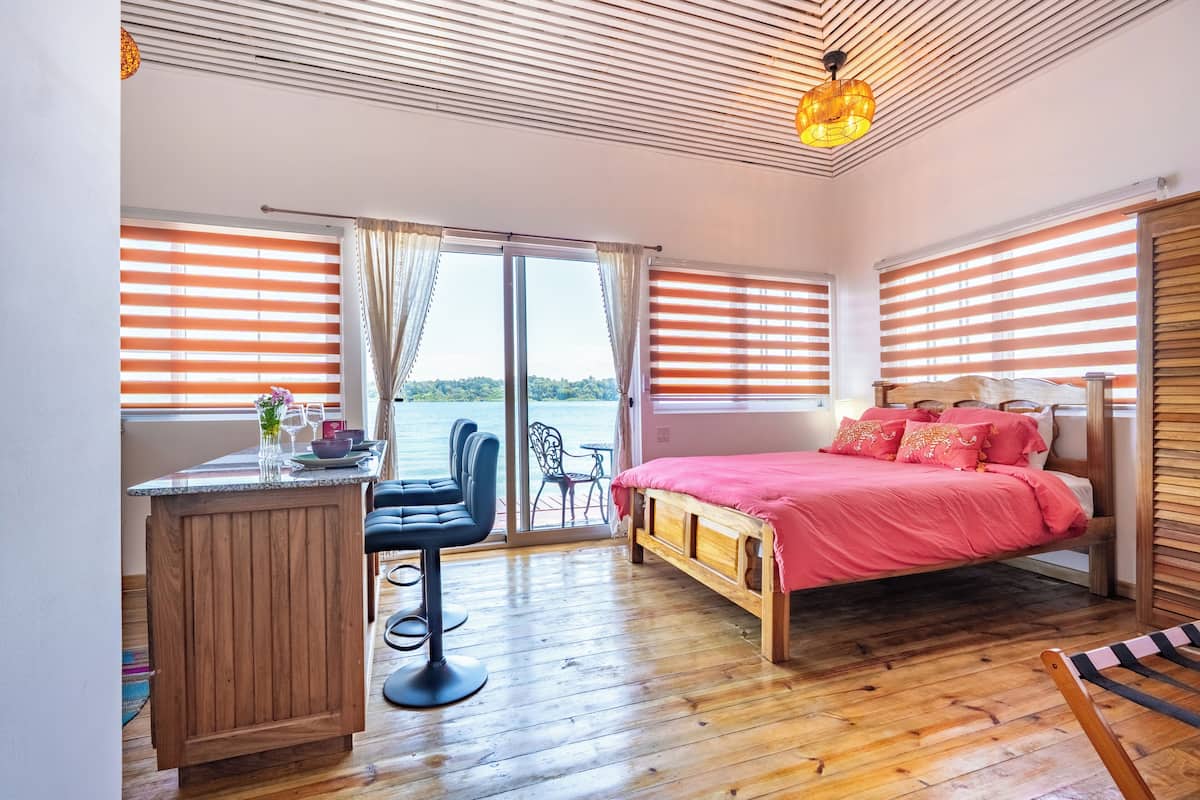 Ein Schlafzimmer mit Bett, Schreibtisch und Stuhl, ein Balkon mit Aussicht und Holzboden.