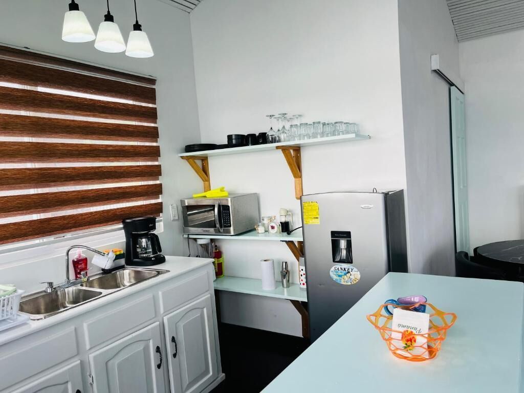 Una cocina compacta con pileta, microondas y refrigerador. Hay estantes sobre el microondas y una mesita con una cesta.
