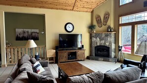 A living room with a wooden ceiling, a stone fireplace, a television, and a sofa. - Gorgeous Donner Lake 3BR + Loft Modern Home in Truckee (Truckee)
