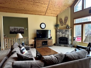 A living room with a wooden ceiling, a stone fireplace, a television, and a sofa. - Gorgeous Donner Lake 3BR + Loft Modern Home in Truckee (Truckee)