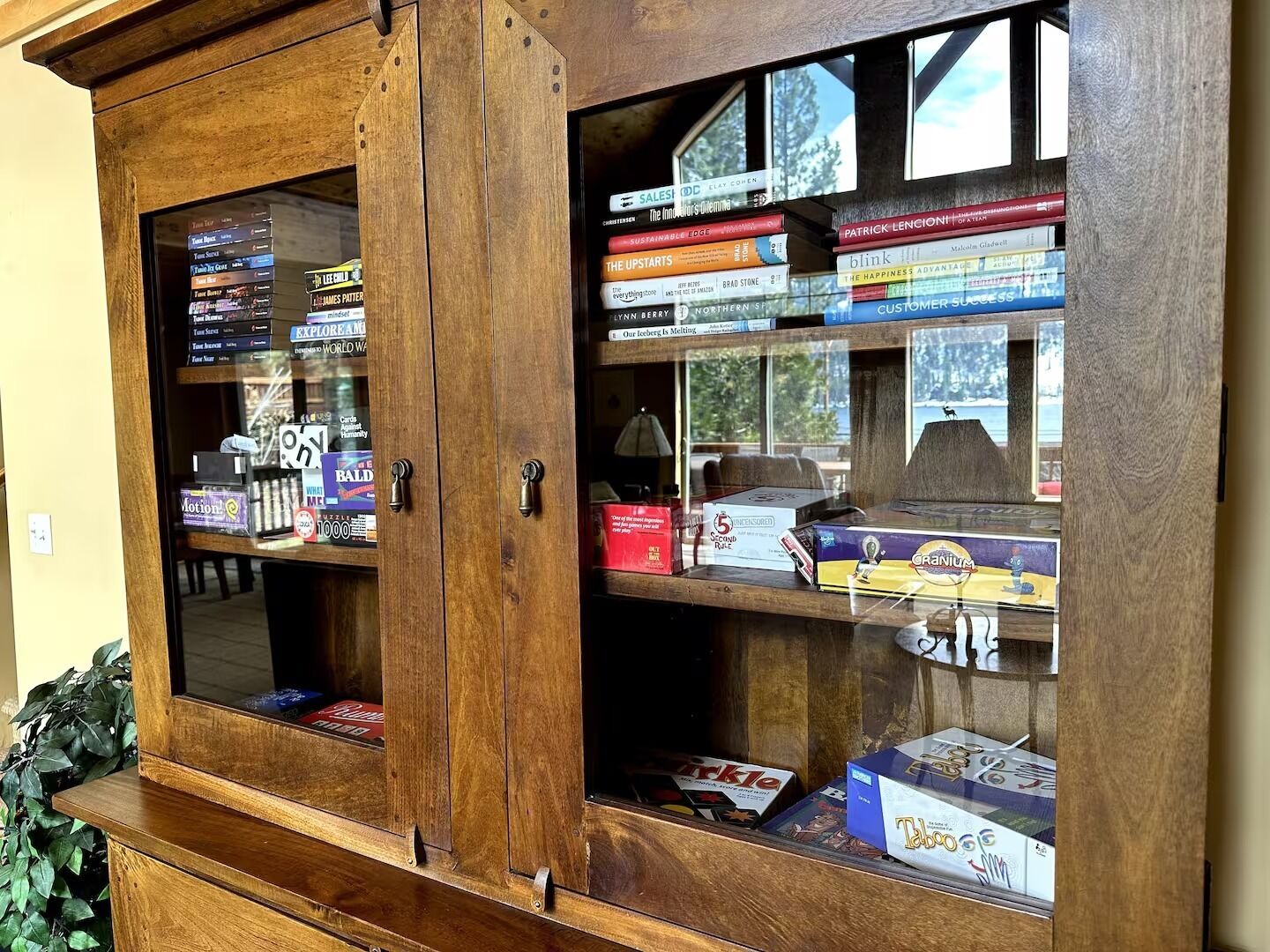 A wooden cabinet with glass doors displaying books and board games.