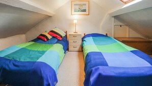 Un pequeño y acogedor dormitorio en el ático con dos camas, una mesita de noche, una lámpara y un tragaluz.