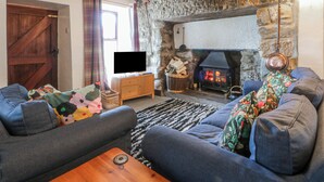 Una sala de estar acogedora con chimenea de piedra, vigas de madera, televisor y un sofá.