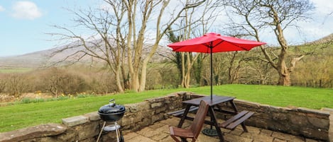 Un patio al aire libre con una parrilla, una mesa de madera, un paraguas rojo y una silla.