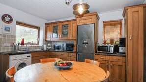Una cocina con armarios de madera, lavadora integrada, una mesa de comedor con sillas y un frutero.