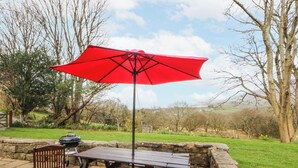 Un patio exterior con mesa y sillas de madera, un paraguas rojo y una parrilla.