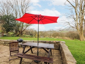 An outdoor patio with a wooden table and chairs, a red umbrella, and a barbecue grill. - Llwyn Y Brig Isaf (Caernarfon)