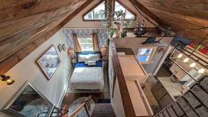 Une chambre de style « loft », avec un lit, un bureau et un escalier.