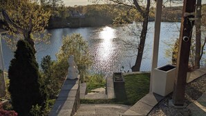 Una escalera de piedra lleva a una terraza con vista a un lago, con una estatua y un porche en primer plano.