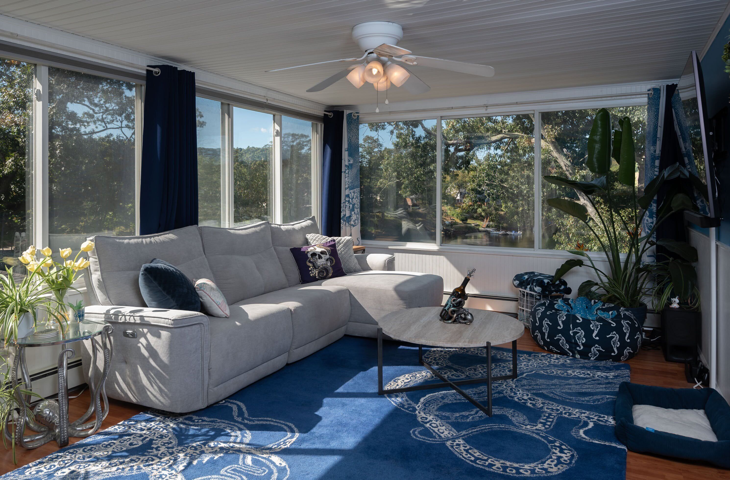 Ein modernes Wohnzimmer mit Sofa, Couchtisch und großen Fenstern mit Blick auf Bäume.