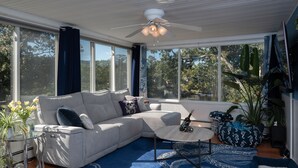 Una sala de estar moderna con un sofá, una mesa de centro y ventanas amplias que dan a un paisaje de árboles.