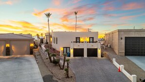 A modern building with a paved driveway, a garage, and a landscaped area with small trees. - Secluded Cottage with Fire-pit & Pool (Lake Havasu City)