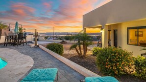 A patio with a pool, outdoor furniture, and a view of the city at sunset. - Secluded Cottage with Fire-pit & Pool (Lake Havasu City)