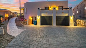 A modern building with a curved facade, a driveway leading to a garage, and a landscaped area with a palm tree. - Secluded Cottage with Fire-pit & Pool (Lake Havasu City)
