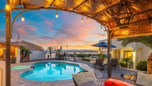 A pool area with a curved pool, lounge chairs, and a covered seating area. - Secluded Cottage with Fire-pit & Pool (Lake Havasu City)