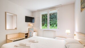 Et hotelværelse med seng, skrivebord, stol, fjernsyn, vindue og en radiator.