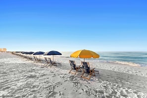 Ein Strand mit Reihen von Liegestühlen und Sonnenschirmen, einem klaren Himmel und dem Meer im Hintergrund.