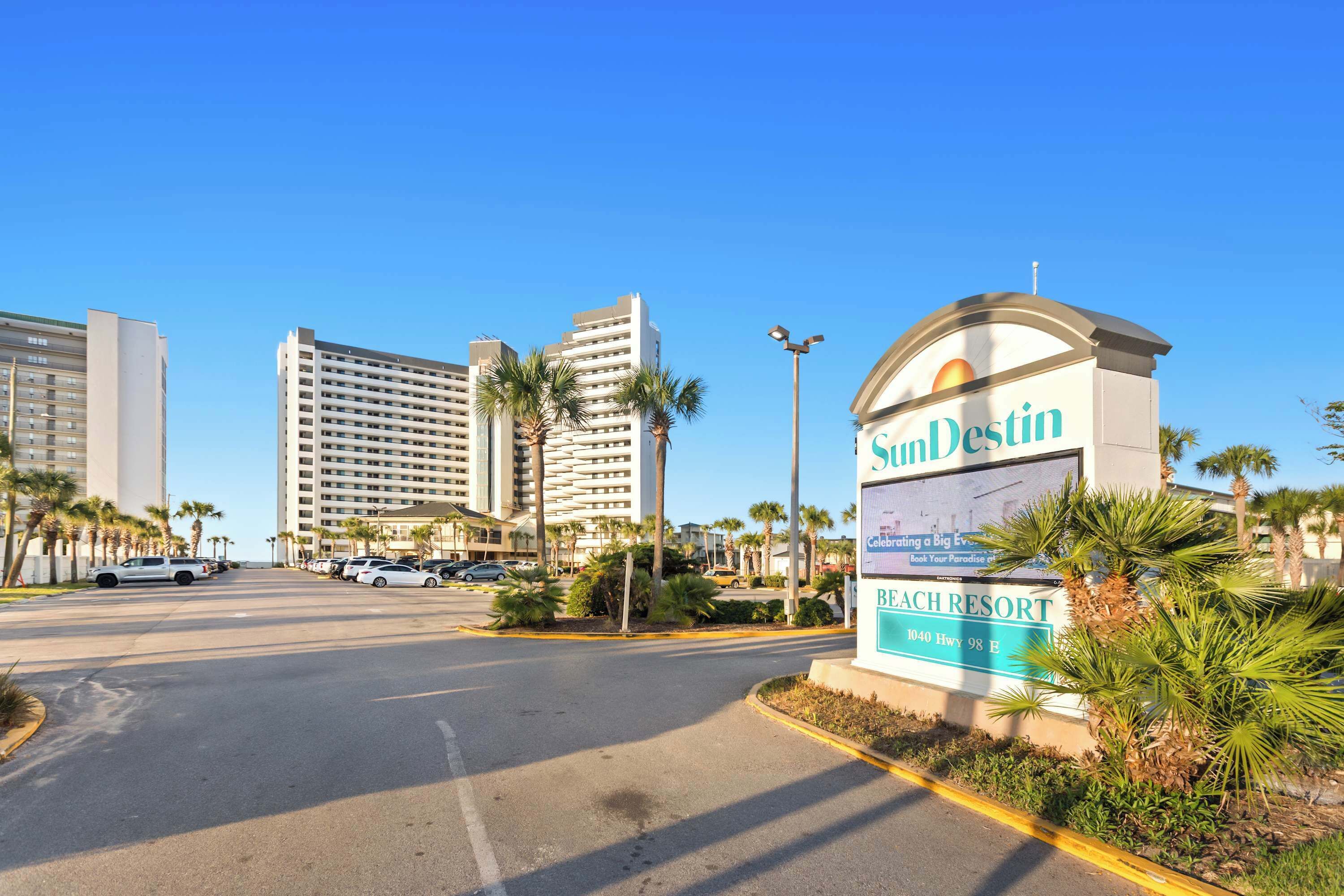 A beach resort sign with palm trees and a clear sky.