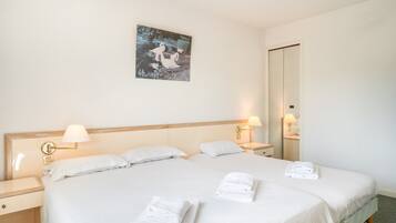 Een tweepersoonsbed met witte lakens, twee nachtkastjes met lampen, een kunstwerk aan de muur en een spiegel.