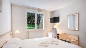 Ein Hotelzimmer mit Bett, Schreibtisch, Stuhl, Fernseher und einem Fenster mit Blick auf Grün.