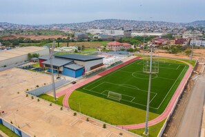 An aerial view of a sports complex with a large green field, a running track, and adjacent buildings.