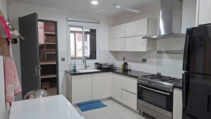 A kitchen with white cabinets, a stove, a refrigerator, a window, and a ceiling fan. - Delightful 3-bedroom apartment in welcoming Accra neighborhood (Accra)