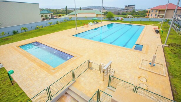 A swimming pool with two separate sections, a sunshade, and a small seating area with chairs and tables. - Delightful 3-bedroom apartment in welcoming Accra neighborhood (Accra)