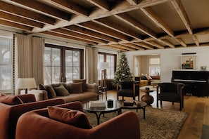 Ein geräumiges Wohnzimmer mit hoher Decke, großen Fenstern, einem Weihnachtsbaum und einem Klavier.