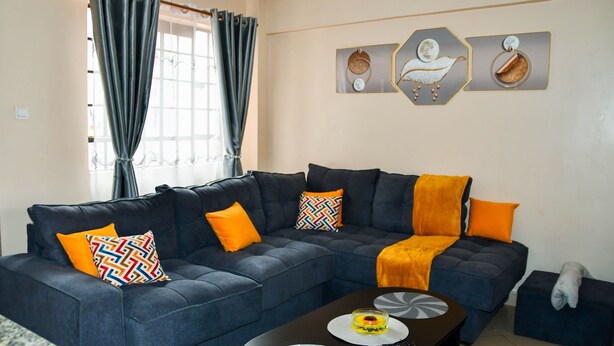 Una sala de estar con un sofá seccional azul oscuro, almohadones naranjas y estampados, una mesa de centro y una obra de arte en la pared.