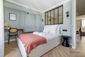 A bedroom with a bed, a bedside table, a chair, a desk, and a large mirror.