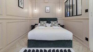 Une chambre à coucher avec un grand lit, deux tables de chevet, une tête de lit et une fenêtre avec des stores.