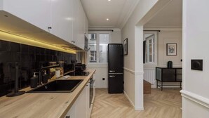 Une cuisine moderne avec un réfrigérateur noir, un plan de travail en bois et une vue sur la salle à manger adjacente.
