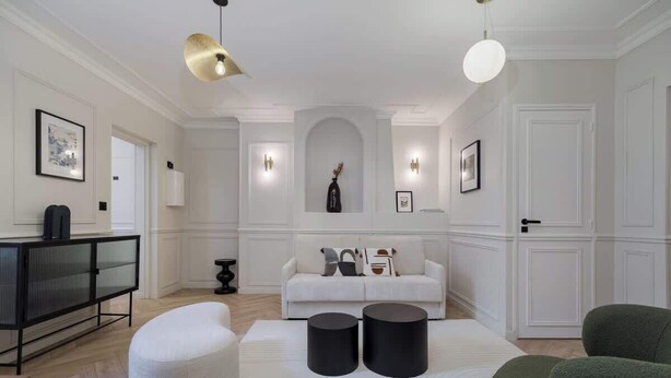 Un salon moderne avec un canapé blanc, deux petites tables d’appoint noires de forme cylindrique et un fauteuil vert.