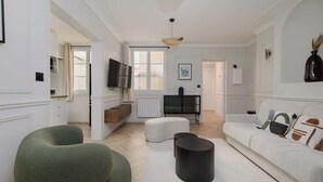Un salon moderne avec un canapé, un pouf et un téléviseur à écran plat.