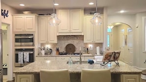 A kitchen with white cabinets, granite countertops, stainless steel appliances, and pendant lighting.