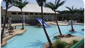 A swimming pool with a slide, palm trees, lounge chairs, and a building with a white roof.