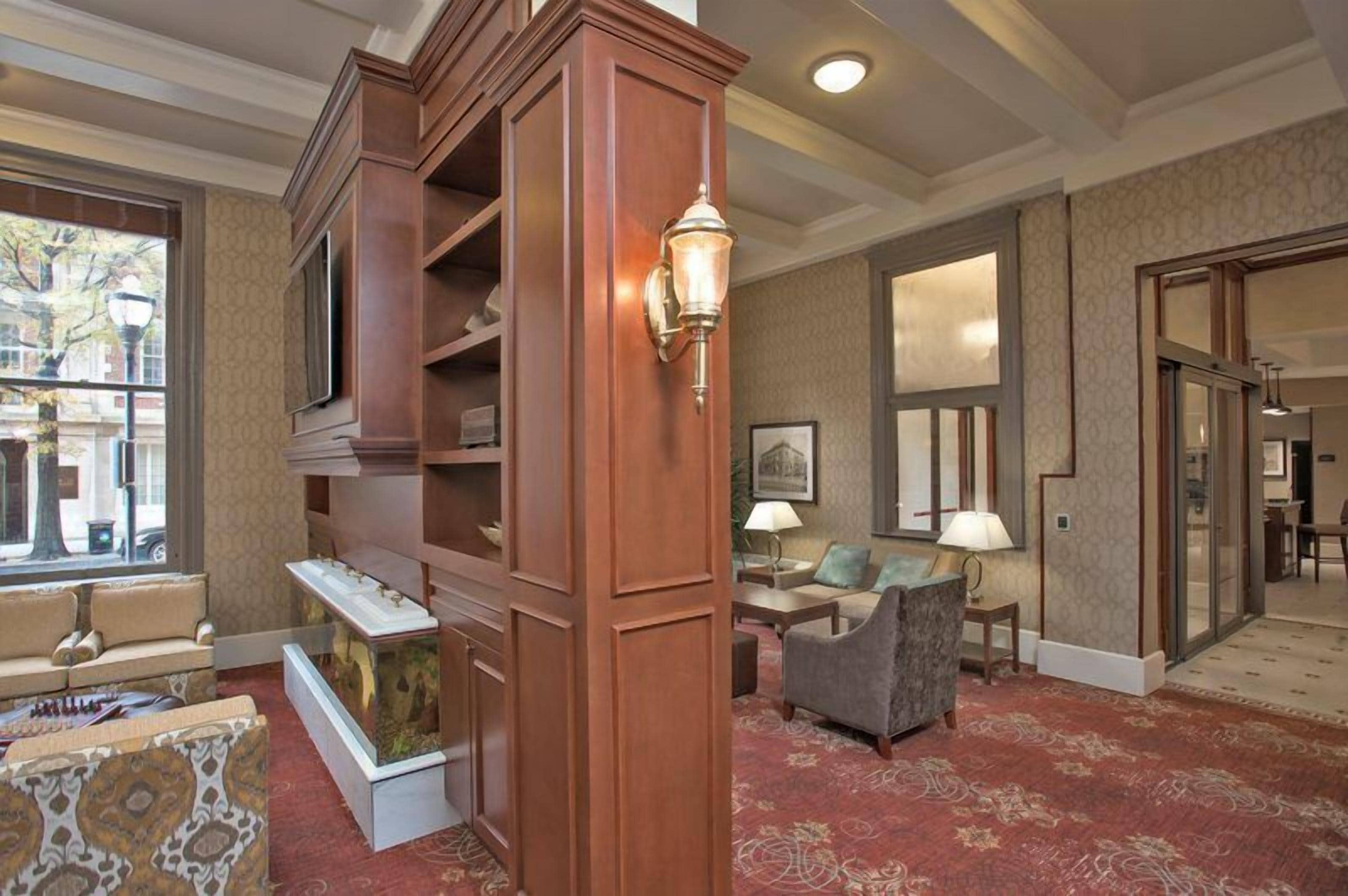 A hotel lobby with a wooden reception desk, a television, a fireplace, and a patterned carpet.