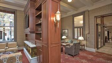 A hotel lobby with a wooden reception desk, a television, a fireplace, and a patterned carpet.