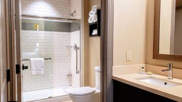 A bathroom with a glass-enclosed shower, a toilet, a sink with a mirror, and a towel rack.
