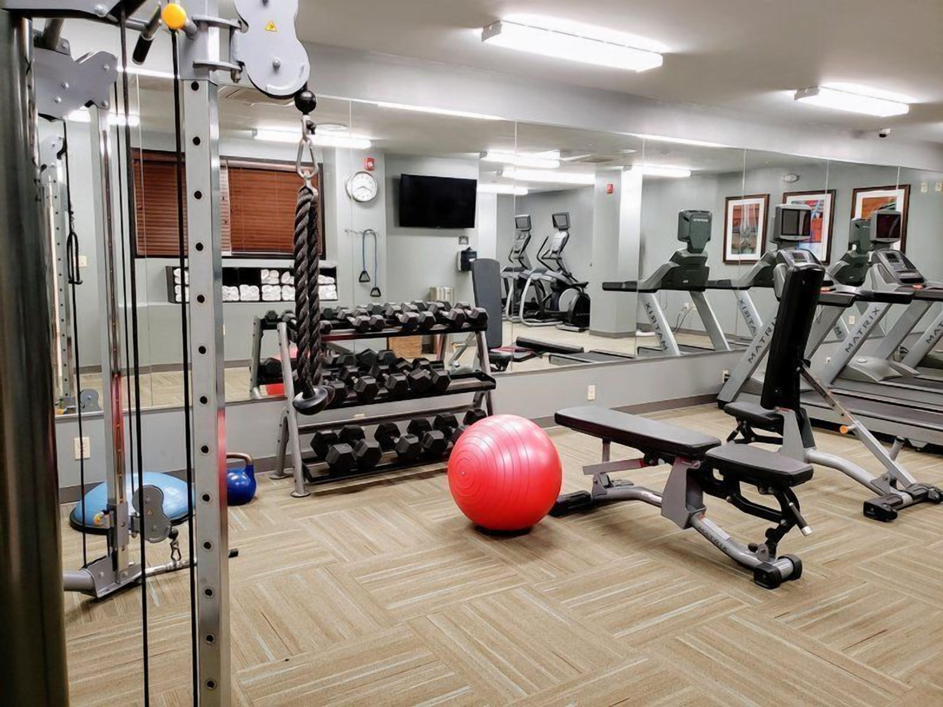 Une salle de sport équipée de matériel d’exercice, avec un ballon rouge et un mur recouvert de miroirs.