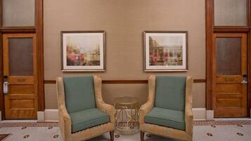 A hotel lobby with two armchairs, a small round table, and two framed pictures on the wall.