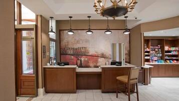 A reception area with a counter, chairs, a chandelier, pendant lights, a large abstract painting, and a bookshelf filled with books.